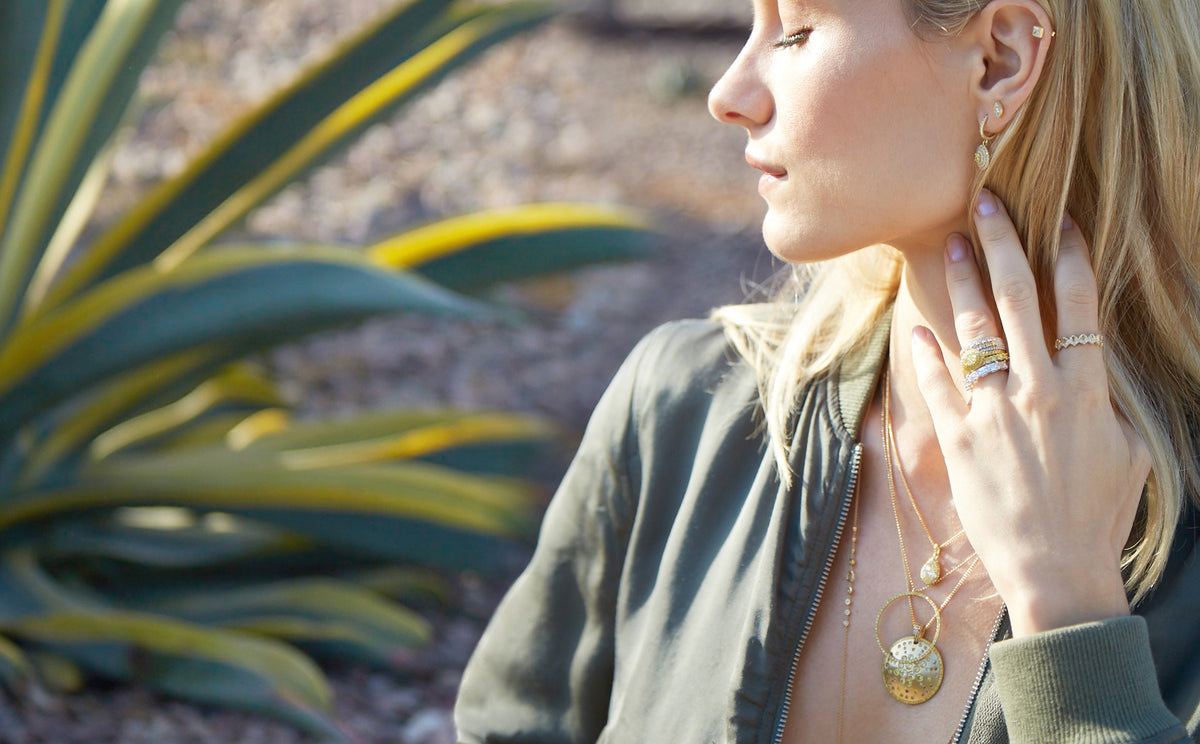 Woman wearing Dominique Cohen yellow diamond, white diamond jewelry while baskin in sun in cactus garden; shop the look; for help, text, call 323-404-2959