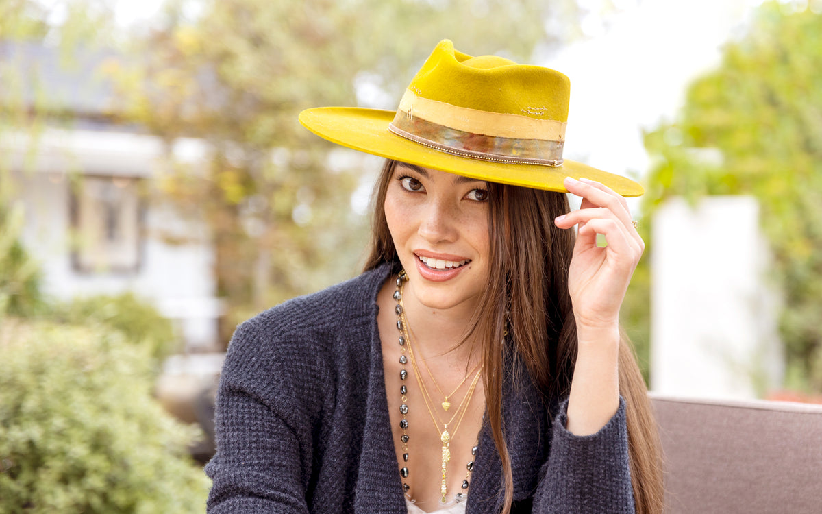 Lovely woman wearing a stylish designer hat in mustard yellow with silk and yellow gold trimmings + 18k yellow gold and yellow diamond jewelry + Tahitian keshi pearl necklace; click to shop; <span class='visuallyhidden'>Call or text 323-404-2959 for assistance</span>
