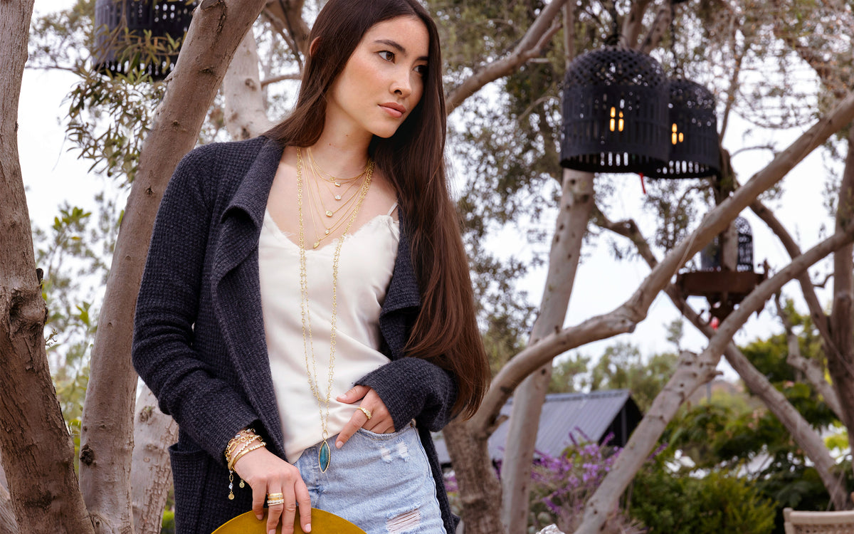 Cascade of white diamond and yellow diamond pendant necklaces + labradorite and diamond enhancer on long chain, all on hip woman in garden; call, text 323-404-2959 for shopping help