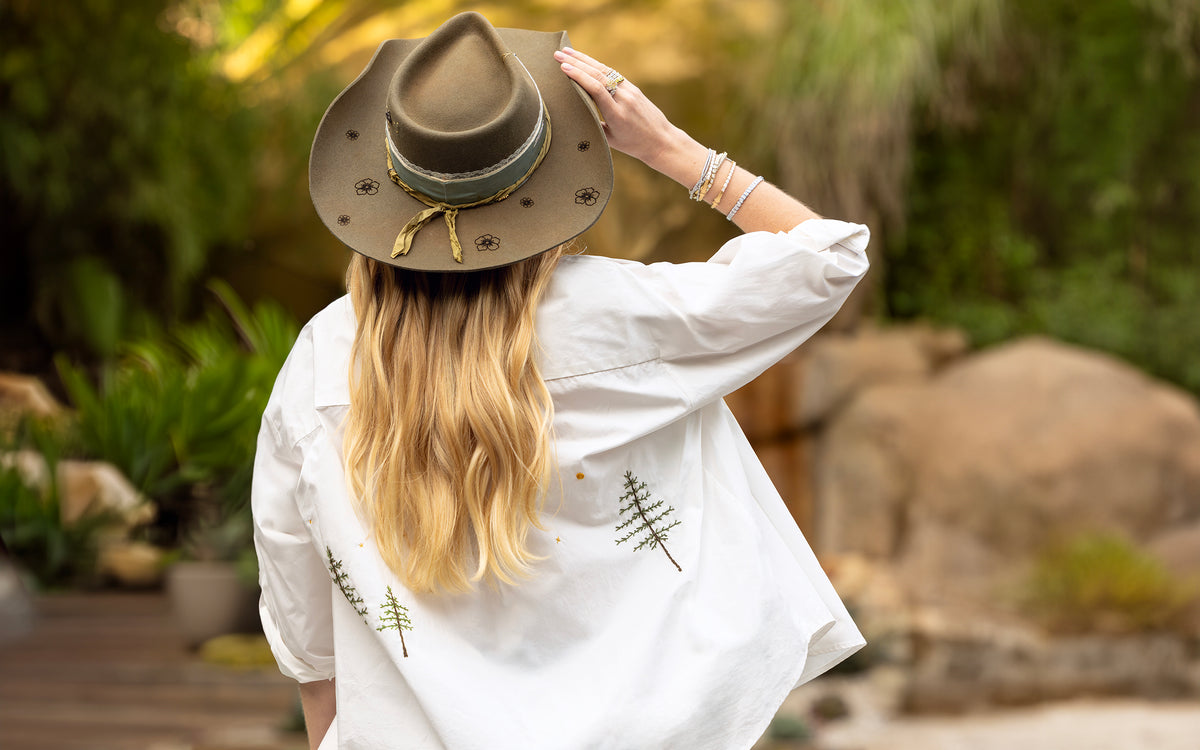 Bespoke hat with flower burns + limited edition embroidered white shirt in conifers theme + diamond bracelets on blonde facing away; 323-404-2959 for shop help