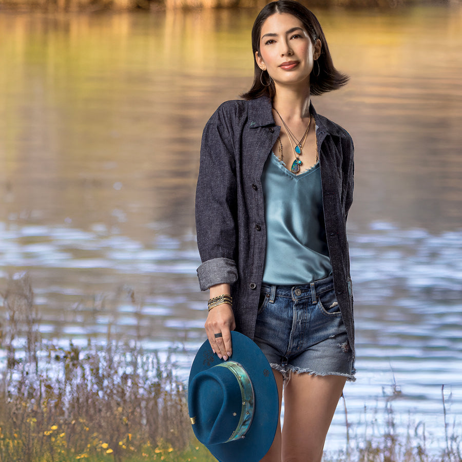 Collection Rhythm and Blues, in diamonds, black gold, yellow gold, Australian opals, and other gemstones, with blue hat and camisole on woman walking in nature; 323-404-2959 for shop help.